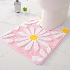 a white toilet sitting next to a pink and yellow flower rug on top of a bathroom floor