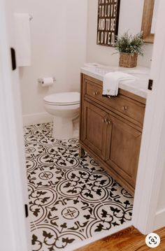 a white toilet sitting in a bathroom next to a wooden cabinet under a mirror on top of a tiled floor