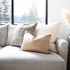 a couch with pillows on it in front of a window and a vase filled with flowers