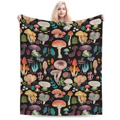 a woman is holding up a black blanket with mushrooms and plants on it in front of her