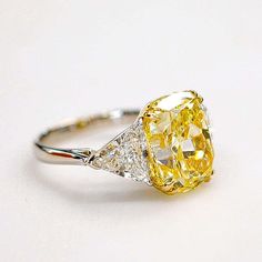 a fancy yellow diamond ring sitting on top of a white table with diamonds around it