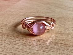 Who doesn't love rose gold? I know I'm in love with it because it's so beautiful and makes unique jewelry looks. This fun ring has a 6mm pink cat's eye wrapped in 20 gauge rose gold colored wire. The wire is silver plated with a tarnish resistant coating to prevent wear and color change. This ring is simple and dainty with a swirl design on either side of the stone. Cat's eye is a beautiful, man made stone with a brilliant flash that dances in the light. Check out the cat's eye section of my sho Adjustable Rose Quartz Rose Gold Ring, Rose Gold Rose Quartz Promise Ring, Wire Wrapped Rose Gold Rings, Cat Eye Bracelet, Jewelry Looks, Cats Eye Ring, Mermaid Glass, Selling Handmade Items, Wire Wrapped Ring