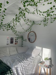 a bed with white sheets and green plants growing on the ceiling in a small room