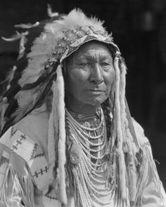 an old black and white photo of a native american man with feathers on his head