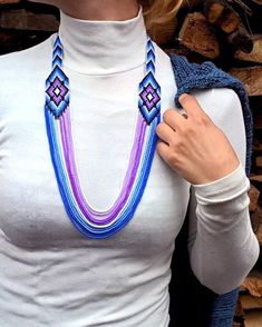 a woman wearing a white shirt and purple necklace with blue beads on her neck, standing in front of firewood logs