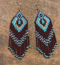 two brown and blue beaded earrings sitting on top of a stone floor next to each other