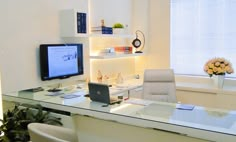 a glass desk with a laptop computer on top of it next to a plant and window