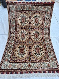 an antique persian rug is displayed on a white tablecloth with fringes around it