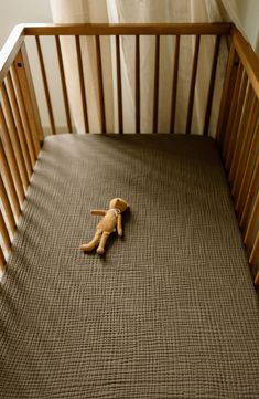 a stuffed animal laying on top of a crib next to a window with curtains