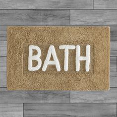 a bath mat with the word bath written in white paint on it, against a wood floor