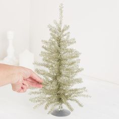 a small white christmas tree is being held by a person's hand in front of it