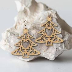 two wooden christmas tree earrings on top of a rock next to a white stone slab