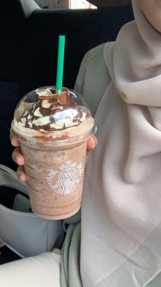 a woman holding up a starbucks drink in her hand and wearing a scarf around her neck