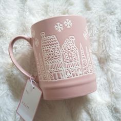 a pink coffee mug with white designs on it and a tag hanging from the handle