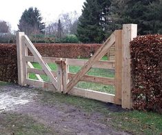 a wooden fence with a gate in the middle of some grass and bushes behind it