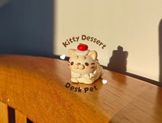 a cat figurine sitting on top of a wooden table next to a sign that says kitty dessert desk pet