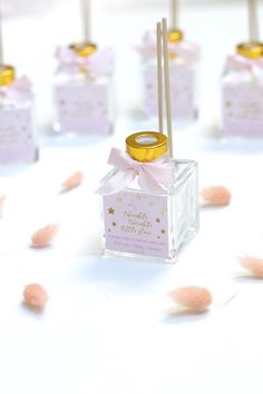 small square glass bottles with gold rims and pink ribbon tied around the top, sitting on a white surface