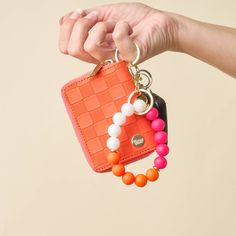 a hand holding an orange and pink purse with beads on the keychain that is attached to it