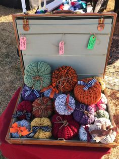 an open suitcase filled with crocheted items on top of a red cloth covered ground