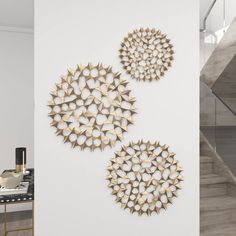 three circular metal sculptures on the wall next to a table and stairs in a white room