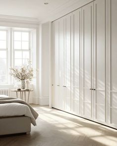 a bedroom with white walls and wooden flooring next to a bed in front of a large window