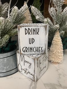 a wooden sign that says drink up grinches merry christmas and white pine trees are in the background