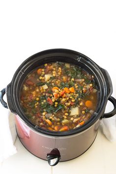 a crock pot filled with vegetable soup on top of a white counter next to a napkin