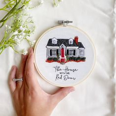 a hand holding a cross stitch embroidery kit with a house and red door on it