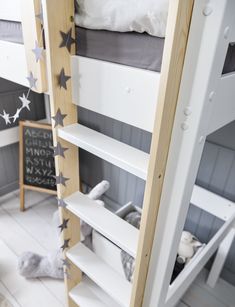 a white bunk bed sitting next to a wooden ladder with stars on the bottom shelf