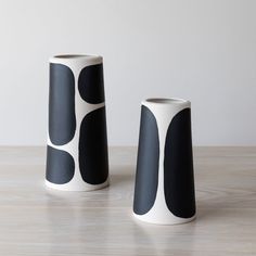 two black and white vases sitting on top of a wooden table next to each other