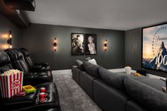 a home theater with grey walls and black couches, two movie screens on the wall