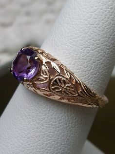 Natural Purple Amethyst Gold Ring Etched Wedding Design#160 Custom This stunning Victorian vintage reproduction ring in 10k rose gold has a brilliant natural purple amethyst gemstone. This full cut round cut genuine amethyst is 6mm in diameter. The inside of the band is marked 10k for gold. Notice the beautiful floral design of the gold filigree setting. This is a lovely rendition of an Antique filigree wedding ring. Make a spectacular statement about love and romance with this glorious solitair Amethyst Rings With Intricate Design For Wedding, Gold Amethyst Ring For Wedding, Gold Amethyst Ring For Wedding, Round Cut, Heirloom Purple Ring For Wedding, Heirloom Purple Rings For Weddings, Classic Lavender Jewelry For Wedding, Heirloom Purple Wedding Rings, Oval Amethyst Filigree Ring For Wedding, Elegant Filigree Amethyst Ring For Wedding