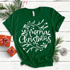 a green t - shirt with the words merry christmas written in white on it next to presents