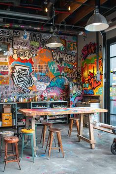 a room filled with lots of graffiti covered walls and wooden tables surrounded by stools