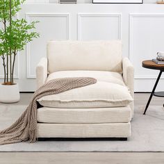 a white chair with a blanket on it next to a table and potted plant