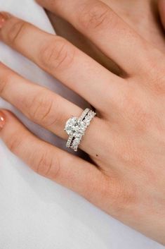 a woman's hand with a diamond ring on top of her finger and the other hand holding an engagement ring