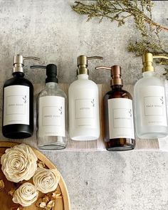 five different types of hand soaps sitting on a table next to flowers and leaves