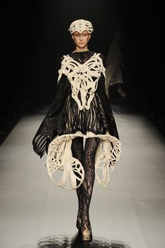 a woman walking down a runway in a black and white dress with lace on it