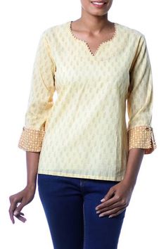 Ritu Agnihotri designs a tunic for elegance and comfort that is sewn of fresh cotton. Leafy branches are block-printed over the beige top featuring long sleeves with brown cuffs for contrast. The tunic's neckline and cuffs are trimmed with white beads. The cuffs feature decorative coconut shell buttons. Yellow Summer Tops With Printed Motifs, Spring Yellow Tops With Printed Motifs, Yellow Chikankari Embroidered Festive Top, Yellow Long Sleeve Top With Chikankari Embroidery, Yellow Long Sleeve Top With Printed Motifs, V-neck Cotton Blouse With Block Print, Festive Yellow Cotton Top, Cotton Kurta With 3/4 Sleeves For Spring, Printed Beige Cotton Blouse