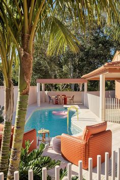 an outdoor swimming pool with lounge chairs and palm trees in the foreground, surrounded by white picket fence