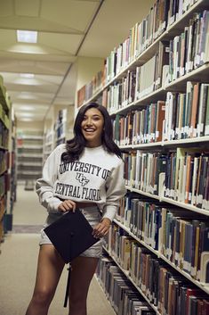 a woman standing in front of a library filled with books and holding a black purse