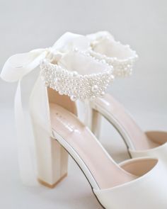 a pair of white high heeled shoes with pearls