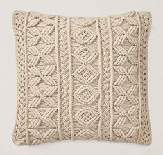 a white pillow with braiding on the front and back, sitting against a wall