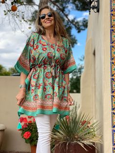 Our Fiji Floral short kaftan is named for Republic of Fiji with its beautiful white beaches and stunning tropical flowers. Jean Marie's beloved uncle Denny lived for 17 years in Fiji, after leaving India, and she recalls fondly his tales of this magical island which she still has yet to visit! This beautiful tropical floral print is hand block printed on lightweight cotton voile. It has a beautiful applied decorative border. It will bring you a little taste of paradise at any time of year. The drawstring tassels are hand beaded and swing gracefully as you stroll along spreading PAX! One size with adjustable drawstring waist Length 32" 100% Cotton lightweight voile Delicate machine wash cold in a lingerie bag to protect tassels or hand wash cold. Hang dry. Made in India This fabric is block Green Short Sleeve Tunic For Vacation, Green Floral Print Vacation Tunic, Green Floral Print Tunic For Vacation, Green Bohemian Kaftan With Floral Print, Green Short Sleeve Kaftan For Vacation, Traditional V-neck Tunic For Vacation, Traditional Green Tunic For Beach, Vacation Green Kaftan With Floral Print, Traditional Green Tunic For Vacation