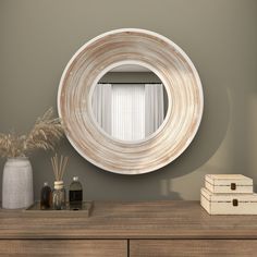 a round mirror sitting on top of a wooden dresser next to a vase and box