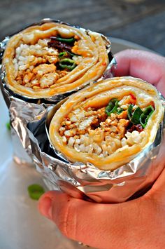 there are two food items wrapped in tin foil on the plate and being held by someone's hand