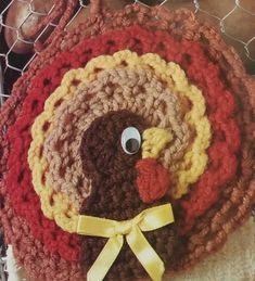 a crocheted turkey hat with a yellow bow on it's head sits in front of a wire fence