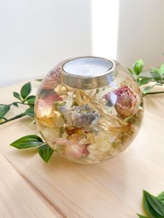 a vase filled with flowers sitting on top of a wooden table next to green leaves