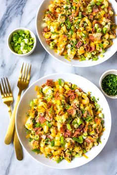 two white bowls filled with corn salad next to silverware and gold forks on a marble surface