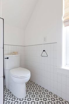 a white toilet sitting next to a window in a room with black and white tiles